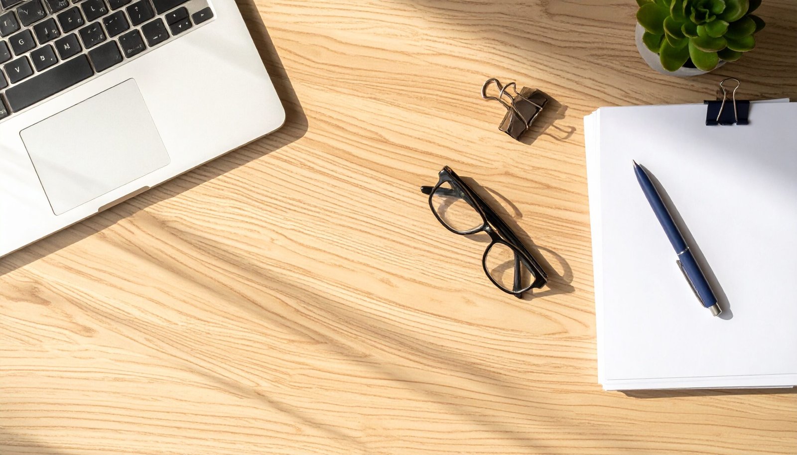 Clean executive desk with laptop, glasses, and documents representing factors that impact business insurance premiums